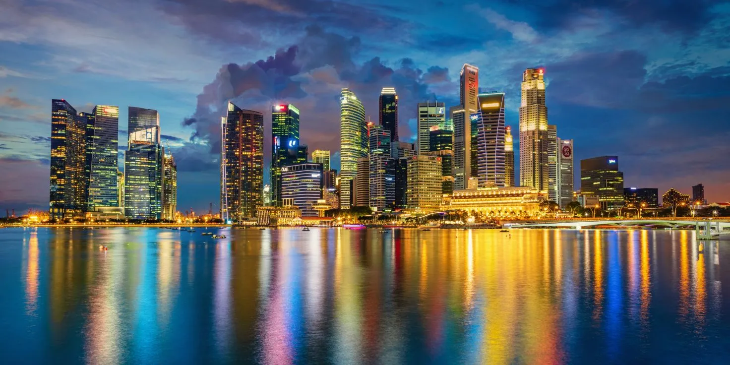 Pamje mahnitëse e një qyteti modern me qiellgërvishtës, me dritat e ndezura që reflektohen në ujë, simbol i një tregu pune global dhe dixhital.