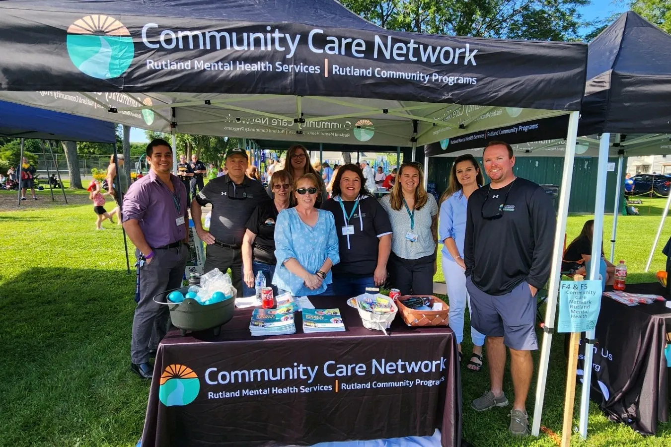 Një grup njerëzish buzëqeshin dhe valëvitin duart në një tubim ndërgjegjësimi “Ec një milje në këpucët e mia”, duke demonstruar solidaritet kundër stigmës së shëndetit mendor.