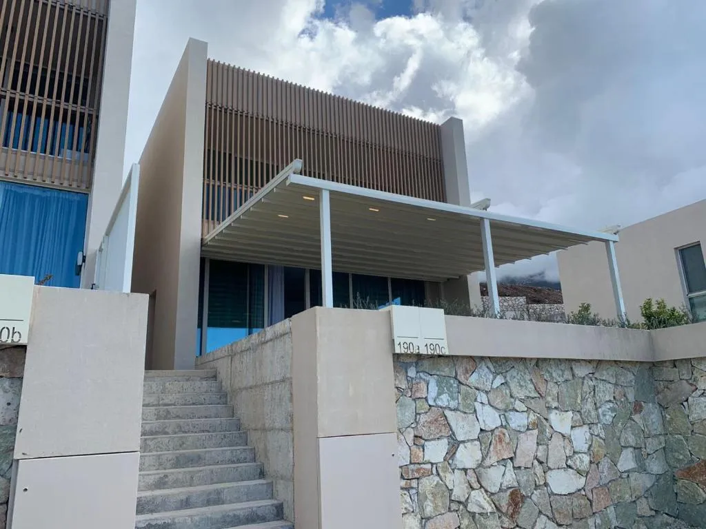 Një shtëpi bashkëkohore me bazë guri, ballkone druri dhe tendë, duke përfshirë materiale lokale dhe hapësira të jashtme.